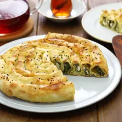Chrupiący borek ze szpinakiem i serem na talerzu, obok filiżanka herbaty.