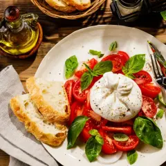 Burrata z pomidorami, bazylią i pieczywem na talerzu.
