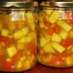 Dwa słoiki z marynowaną cukinią w zalewie curry z kawałkami papryki i gorczycą.