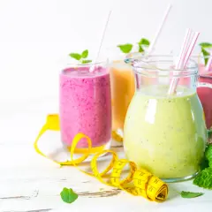 Kolorowe koktajle odchudzające w dzbanku i szklankach, ozdobione miętą i miarką krawiecką.