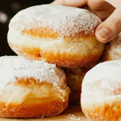 Stos pączków oprószonych cukrem pudrem, jeden jest podnoszony ręką.