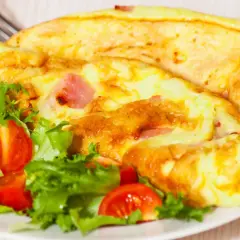 Złocisty omlet z szynką i pomidorkami koktajlowymi na talerzu z sałatą.