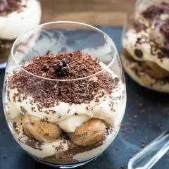 Deser tiramisu w szklance, posypany startą czekoladą i ziarnami kawy.