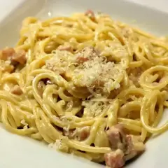 Porcja spaghetti carbonara z kawałkami boczku i startym parmezanem.