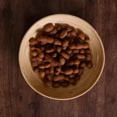 Tamaryndowiec w łupinie w drewnianej misce na ciemnym tle.