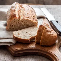 Chleb pokrojony na desce, obok nóż i lniana ściereczka.