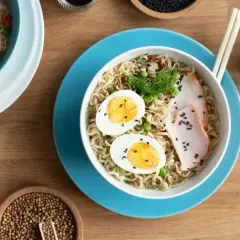 Dwie miski z makaronem, jedna z jajkiem i plastrami mięsa, druga z grzybami. Pyszny tantanmen na drewnianym stole.