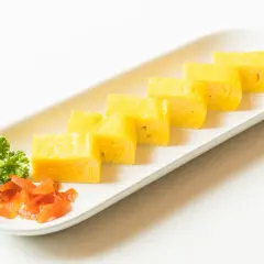 Japoński omlet tamagoyaki pokrojony w plastry, podany z natką pietruszki i marynowaną marchewką.