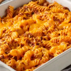 Zapiekanka makaronowa z mięsem mielonym w sosie śmietanowym, pokryta roztopionym, ciągnącym się serem cheddar.