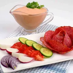 Sos do kebaba w sosjerce, obok talerz z warzywami i róża z salami.