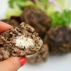 Kotlet mielony z serem w środku, trzymany w dłoni, na talerzu z sałatką.