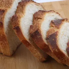 Pokrojony bochenek chleba z chrupiącą skórką na drewnianej desce.