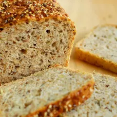 Domowy chleb z ziarnami, przekrojony bochenek i kromki na drewnianym tle.