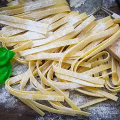 Świeży makaron tagliatelle posypany mąką, z listkami bazylii i drewnianą łyżką.