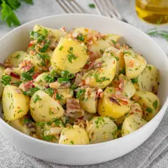 Sałatka ziemniaczana z boczkiem, cebulką i ziołami w białej misce.