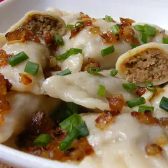 Pierogi z mięsem posypane skwarkami i szczypiorkiem.