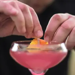 Dłonie barmana ozdabiają drinka skórką pomarańczy. To klasyczny cosmopolitan, gotowy na wieczór w wielkim mieście.