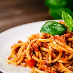 Talerz spaghetti z ragù mięsnym, posypany parmezanem i udekorowany listkami bazylii.