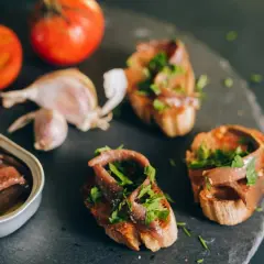 Otwarta puszka anchois, bruschetty z anchois i natką pietruszki, pomidory i czosnek na ciemnym tle.