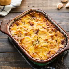 Zapiekanka z ziemniakami i mięsem mielonym w naczyniu żaroodpornym, ozdobiona rozmarynem.