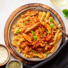 Pyszny makaron z kurczakiem w sosie pomidorowym, udekorowany bazylią. Obok miseczki z parmezanem i ziołami.