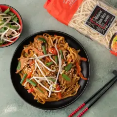 Talerz makaronu chow mein z warzywami i kiełkami fasoli, obok paczka makaronu i miseczka kiełków.