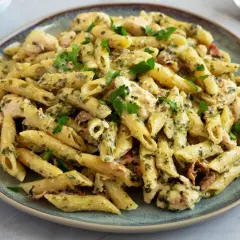 Kremowy makaron penne z kurczakiem, szpinakiem i suszonymi pomidorami, udekorowany natką pietruszki.
