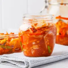 Słoiki i naczynie szklane wypełnione pikantnym, pomarańczowym kimchi.