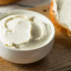 Kremowy serek, idealny serek philadelphia zamiennik, w białej miseczce obok posmarowanej kromki pieczywa.