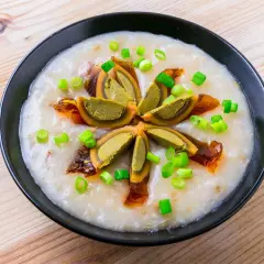 Miseczka z congee, ozdobiona połówkami jajka stuletniego, posypana szczypiorkiem i skropiona olejem chili.