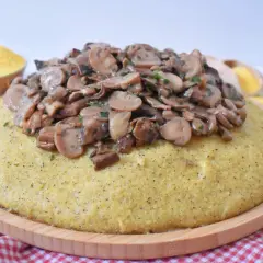 Polenta z duszonymi pieczarkami na drewnianej desce, obok miseczka mąki kukurydzianej.