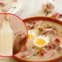 Miseczka żurku z jajkiem i kiełbasą, obok butelka zakwasu, czosnek i chleb.