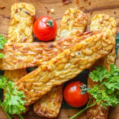 Usmażony tempeh z pomidorkami koktajlowymi i natką pietruszki na drewnianym tle.