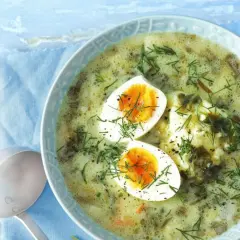 Zupa szczawiowa z jajkiem i koperkiem w misce, obok chochla.
