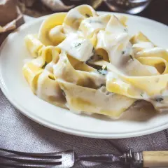 Makaron tagliatelle w kremowym sosie serowym z ziołami na białym talerzu.
