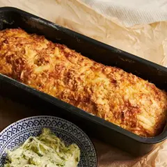 Złocista babka ziemniaczana z serem, prosto z piekarnika, pachnie jak babcia. Obok miseczka z ziołowym masłem.