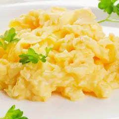 Kremowa jajecznica z serem i natką pietruszki na białym talerzu.