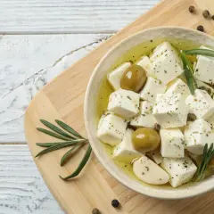 Kostki sera feta w oliwie z oliwkami, czosnkiem i rozmarynem na desce.