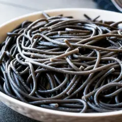 Czarny makaron spaghetti w białej misce, zbliżenie.