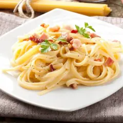 Talerz spaghetti carbonara z boczkiem i natką pietruszki, na lnianej serwetce.