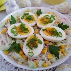 Sałatka z paluszkami krabowymi, jajkiem, kukurydzą i ogórkiem, ozdobiona szczypiorkiem.