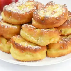 Puszyste racuchy z jabłkami posypane cukrem pudrem na białym talerzu.