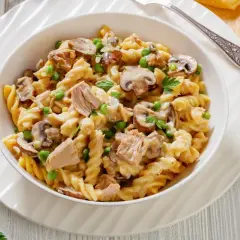 Makaron fusilli z tuńczykiem, groszkiem i pieczarkami w kremowym sosie, udekorowany natką pietruszki.