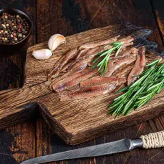 Filety anchois z rozmarynem i czosnkiem na drewnianej desce.