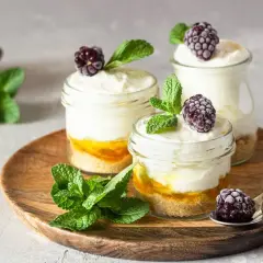 Pyszny keto deser w słoiczkach z warstwami kremu, owoców i chrupiącego spodu, ozdobiony jeżynami i miętą.