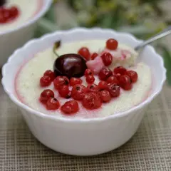 Kasza manna z wiśniami i porzeczkami w białej miseczce.