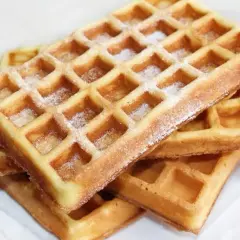 Stos domowych, idealnie chrupiących gofrów posypanych cukrem pudrem.