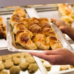 Taca z croissantami, którą trzymają ręce, na tle innych wypieków.
