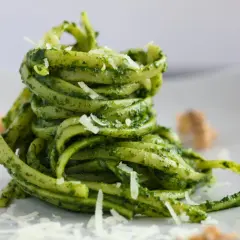 Makaron tagliatelle z zielonym pesto bazyliowym i startym parmezanem na białym talerzu.