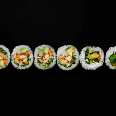 Sześć grubych rolek sushi futomaki z widocznym nadzieniem na czarnym tle.